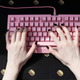 A gamer with black painted nails types on an all-pink keyboard.